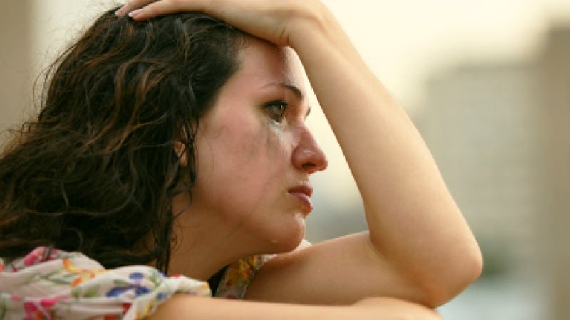 Mujer llorando mirando por una ventana triste