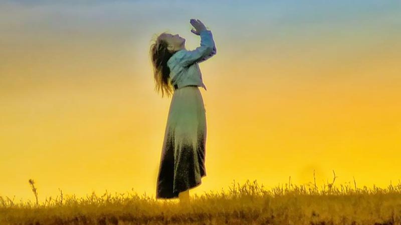 Mujer orando a Dios en pie al aire libre y levantando sus manos