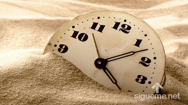 Reloj enterrado en la arena, concepto de postergar, posterga